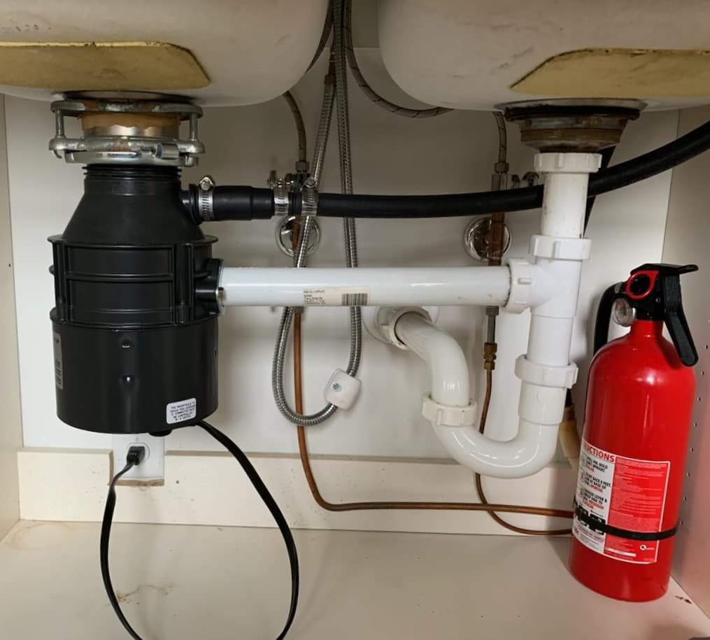 Picture of a double sink and new pvc piping under the sink that connects to a garbage disposal 